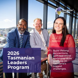 Photo of three TLP participants from 2023. A woman with long black hair and a long sleeved red dress, a fair haired man with a beard in a grey suit jacket and a dark haired man in a blue suit leaning on a small table together. View behind them overlooks the city of Hobart.
