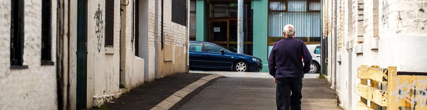 photo of a man walking up an alleyway facing away from the viewer
