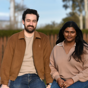 a man with a beard and a women with long dark hair sitting on a bench facing the viewer