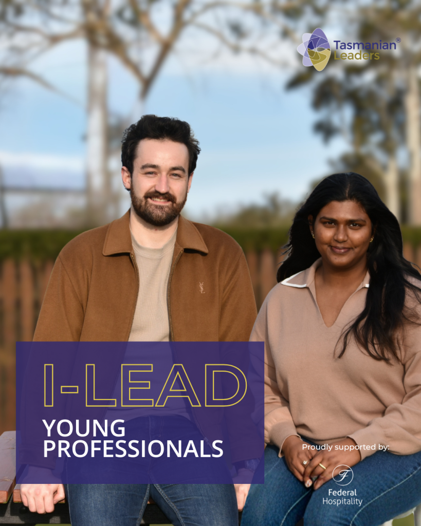two people sitting on a bench - a man with a beard and fair skin, the woman with long dark hair and dark skin, a fence and bush landscape is behind them